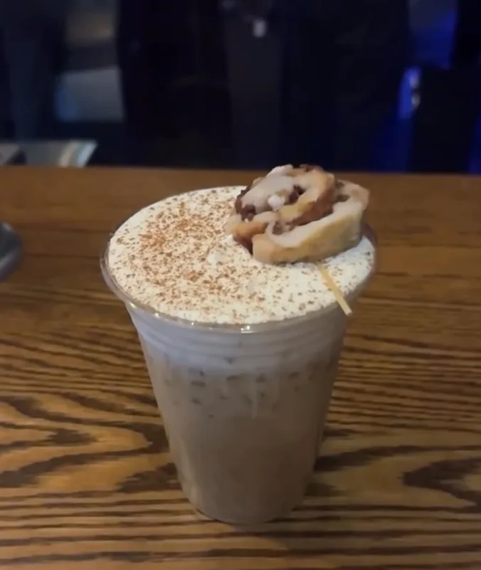 An iced latte topped with cream, cinnamon and a mini cinnamon roll