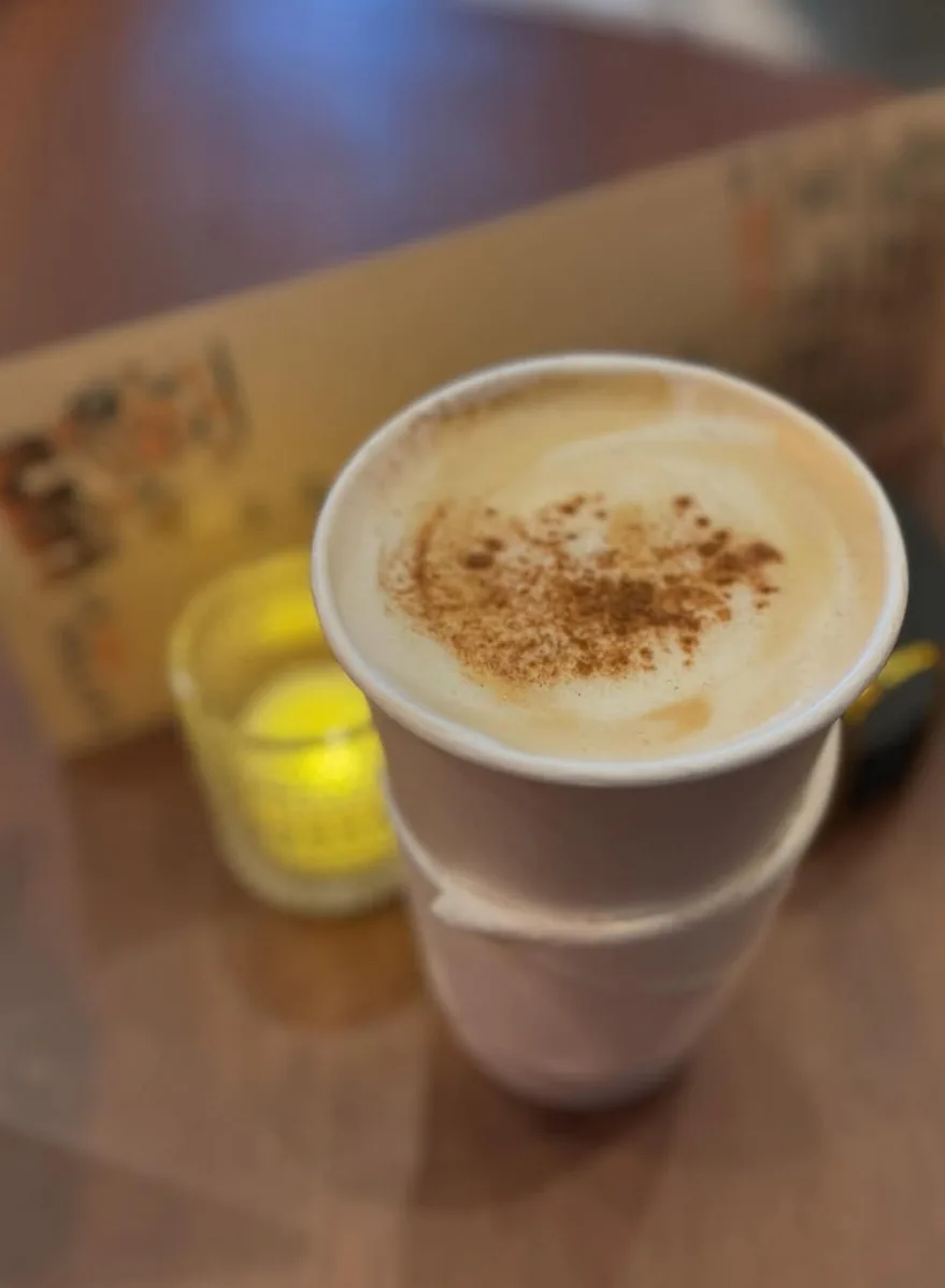 A hot latte dusted with cinnamon beside a lit candle on a wooden table