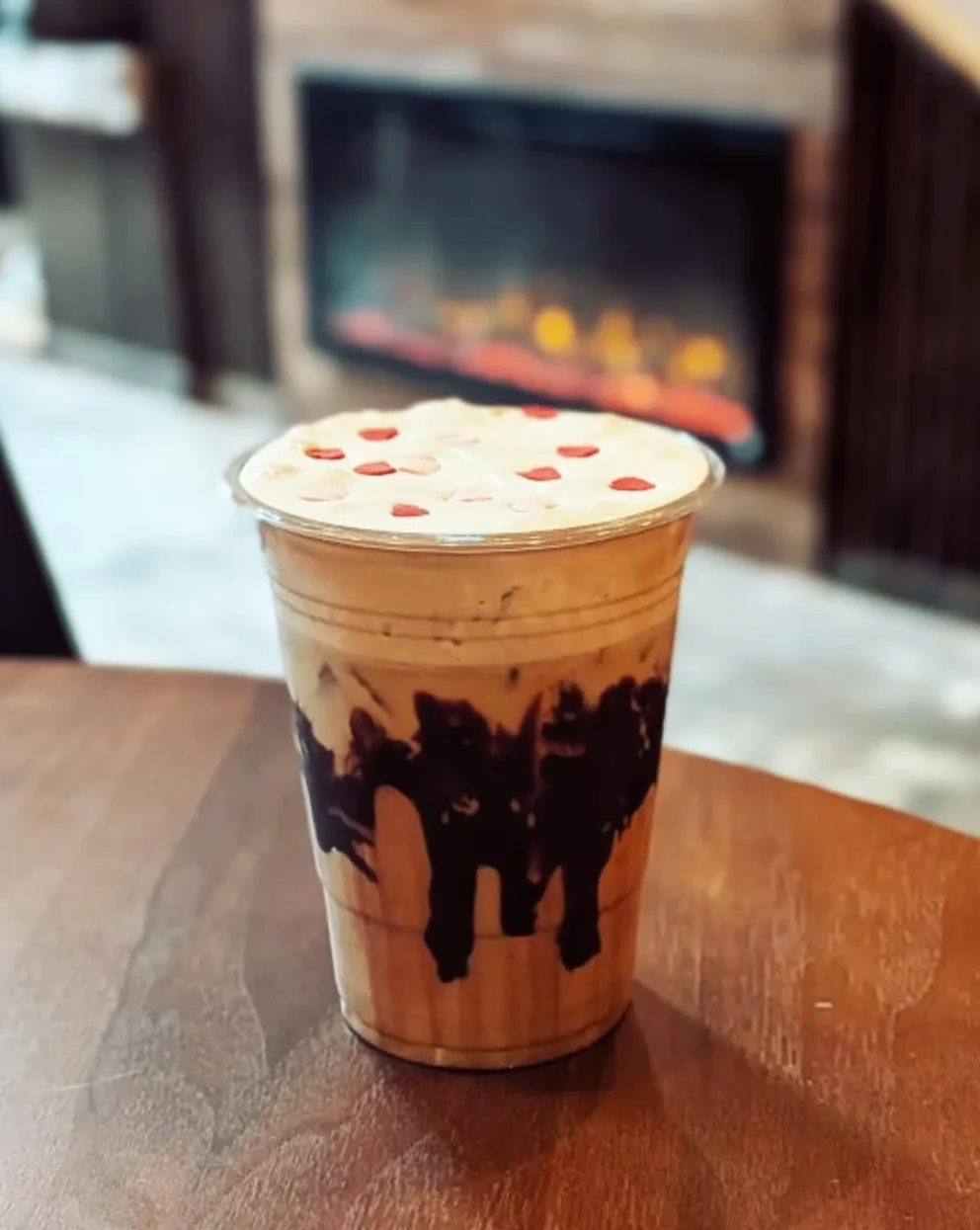 An iced strawberry mocha with chocolate drizzle in front of a fireplace at Lee's Coffee