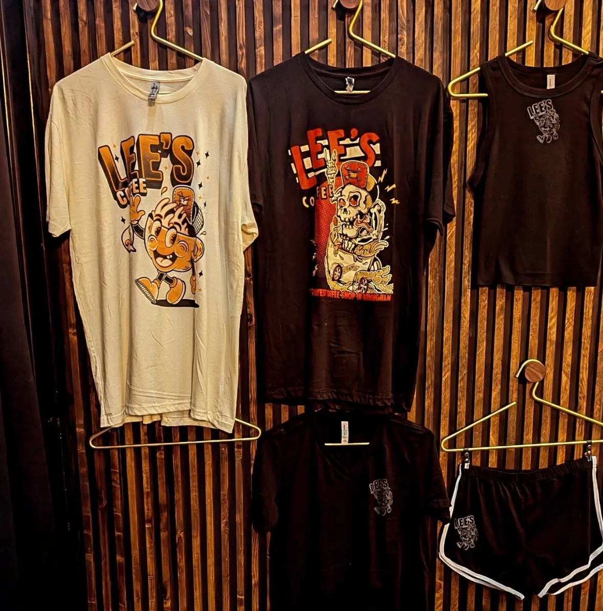 Lee's Coffee t-shirts and shorts hanging on a slatted wood wall