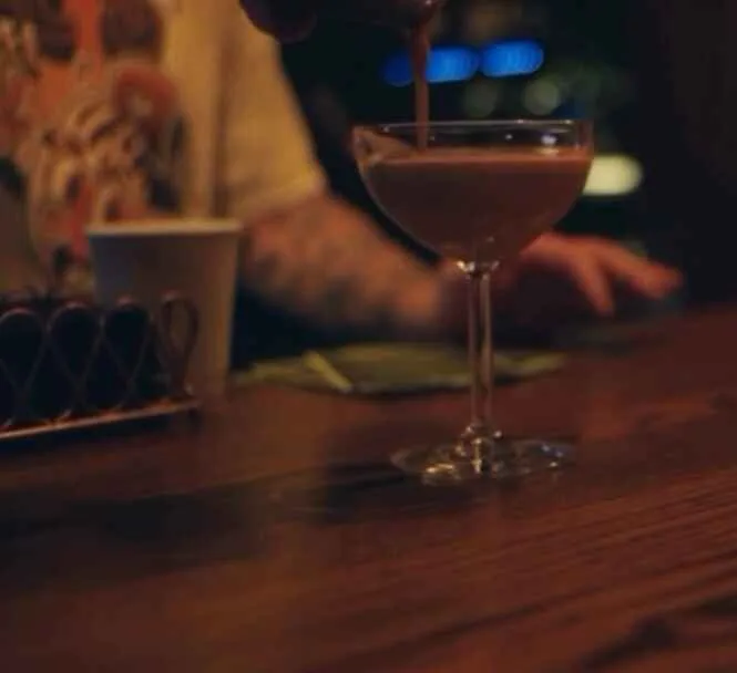 A cocktail being poured into a coupe glass at the bar at Lee's